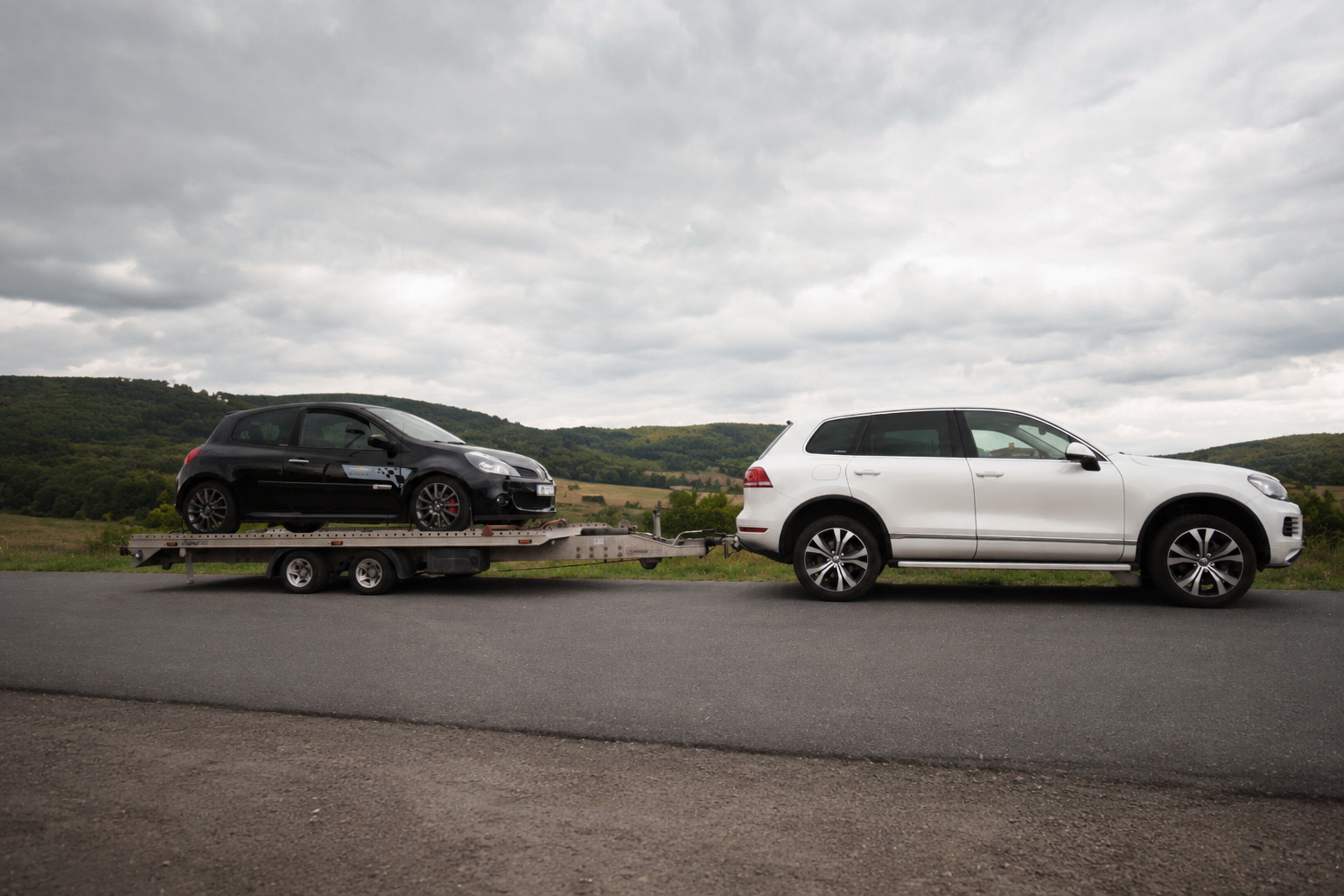 Bílý Volkswagen Touareg s přívěsem přepravující černý vůz