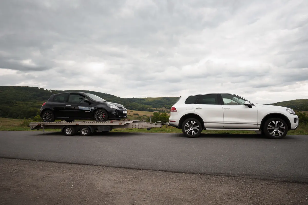 Bílý Volkswagen Touareg s přívěsem přepravující černý vůz